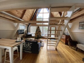 A cozy loft bedroom with a wooden ceiling, a large window, a Christmas tree, a ladder, and a dog. - Mod A Frame Cabin in the Woods with Hot Tub -close to Mt. Snow & Stratton! (Wardsboro)