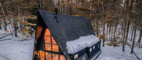 A cabin with a sloped roof, a deck, and a hot tub in a snowy forest.