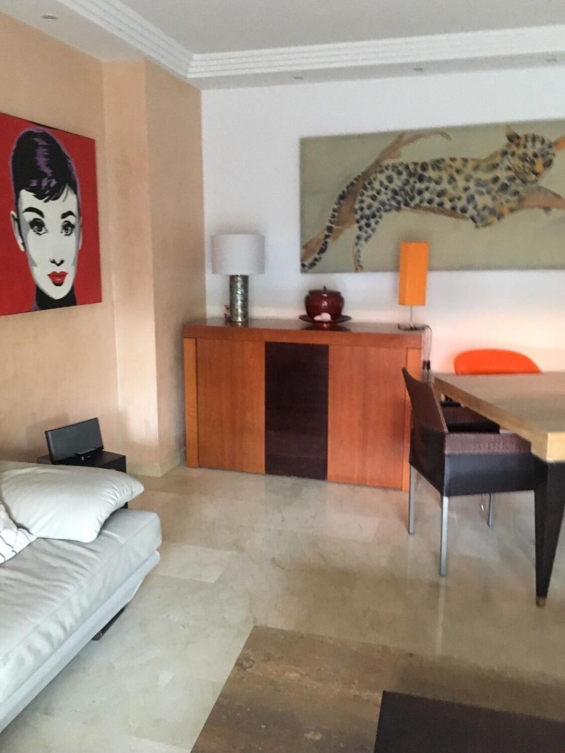 A modern living room with a sofa, a dining table, a TV, a lamp, and artwork on the walls.