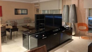 Ein modernes Wohnzimmer mit großem Flachbildfernseher, einer Couch, einem Couchtisch und einem Essbereich mit Stuhl und Tisch.