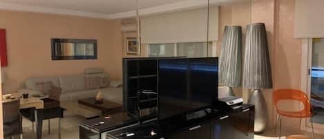 Una sala moderna con un televisor de pantalla plana grande, un sofá, una mesa de centro y una zona de comedor con una silla y una mesa.