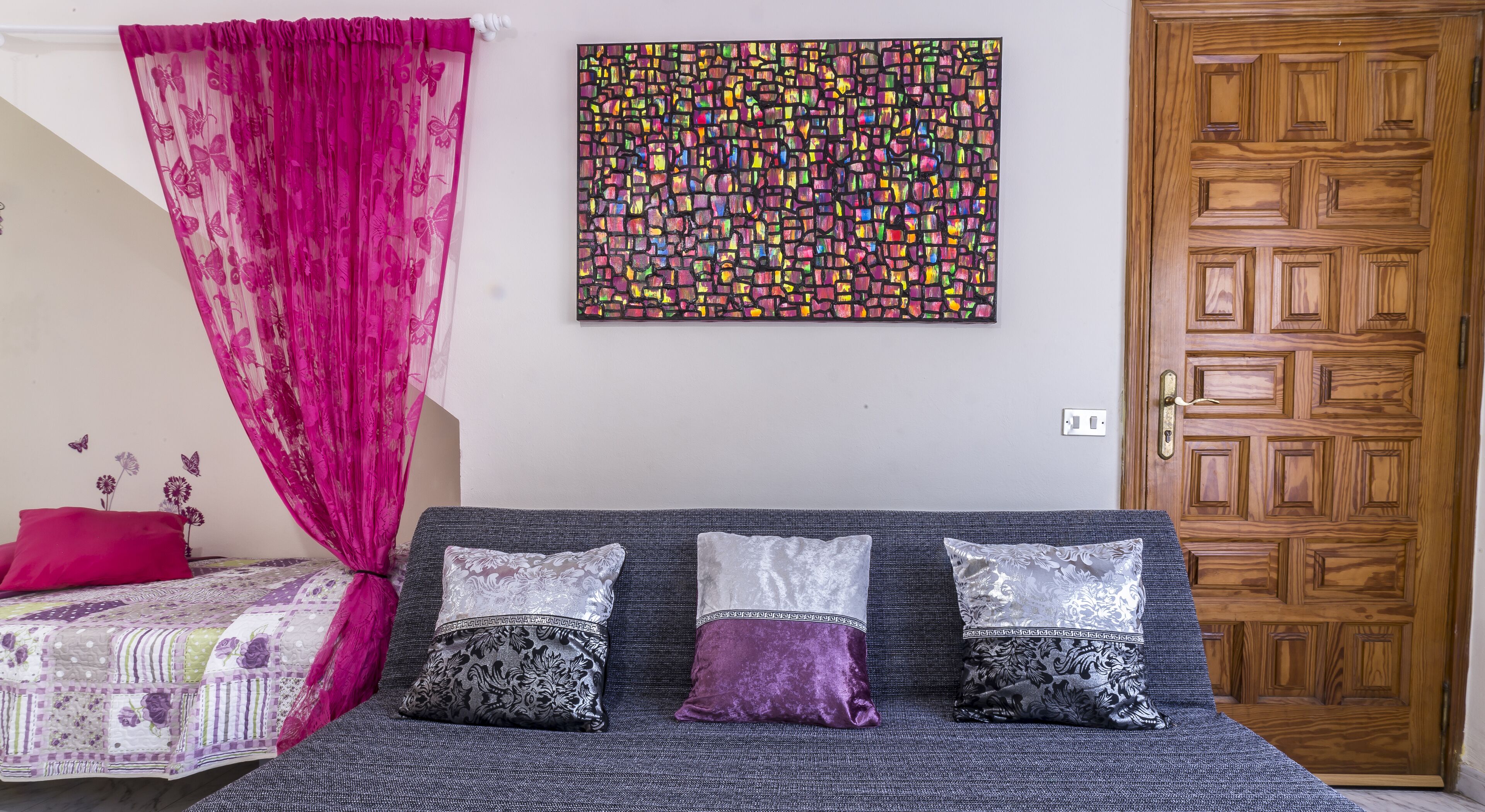 Une chambre à coucher avec un lit, une porte en bois et un tableau abstrait aux couleurs vives accroché au mur.