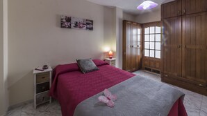A bedroom with a bed, a nightstand, a lamp, a window, and wooden wardrobes. - Vacational Housing CAÑAMO, Feel the Quiet Difference .... (Tamaduste)