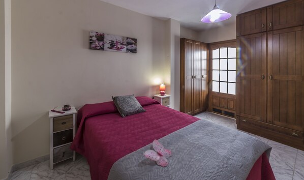 A bedroom with a bed, a nightstand, a lamp, a window, and wooden wardrobes.