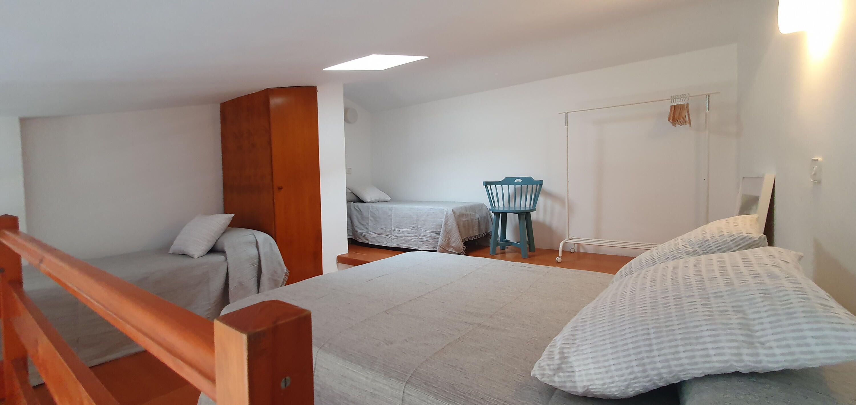 A bedroom with two beds, a wooden wardrobe, a chair, and a wardrobe with a mirror.
