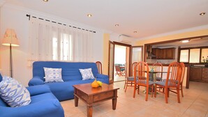 Een woonkamer met een blauwe bank, een houten salontafel en een eethoek met houten stoelen en een tafel.