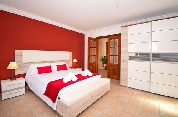 Un dormitorio con una cama grande, paredes rojas, un armario de madera y una mesita de noche con lámpara.