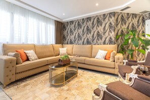 A modern living room with a beige sofa, a glass coffee table, and a patterned wall.