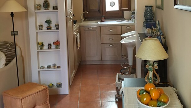 A compact kitchen with a central island, a dining area with a table set for two, and a cozy seating area with a cushioned stool. - Apartment in Taormina center (Taormina)