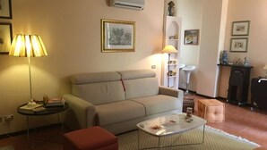 A living room with a sofa, a coffee table, a red ottoman, a lamp, and a framed picture on the wall. - Apartment in Taormina center (Taormina)
