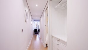 Un couloir étroit avec un plancher en bois, des murs blancs et une armoire blanche dotée de tiroirs.