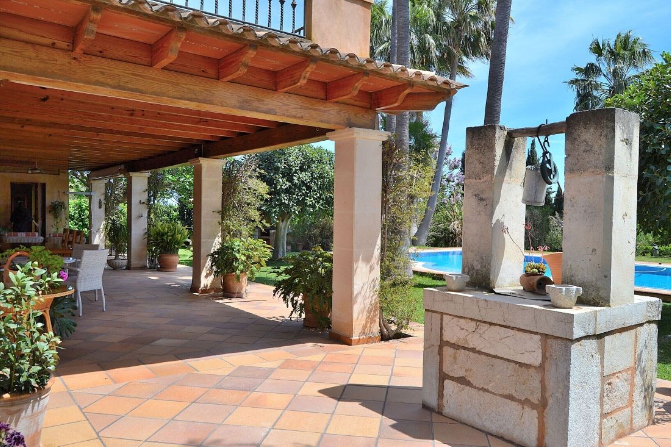 An outdoor patio area with a tiled floor, wooden pergola, and potted plants.