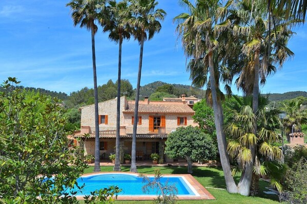 Una villa de piedra con piscina, rodeada de palmeras y vegetación.