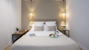 Un letto rifatto con cura, coperto da una trapunta fantasia, due abat-jour, un comodino con una pianta, un vassoio con prodotti per la colazione e una rivista sul letto.