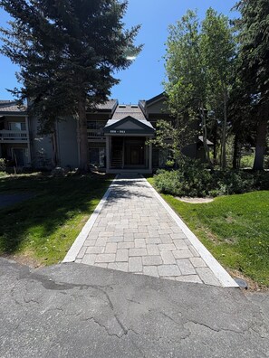 A building with a paved walkway leading to the entrance, surrounded by trees and grass.
