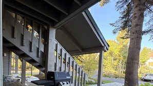 Ein überdachter Außenbereich mit Grill, Holzterrasse und Blick auf einen Baum und eine Straße.