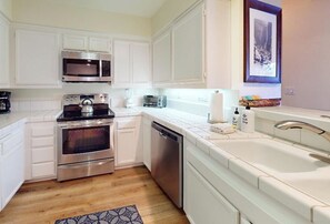 A compact kitchen with white cabinetry, stainless steel appliances, and a built-in dishwasher.