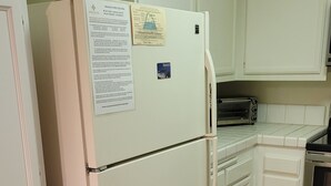 Eine Küche mit weißen Schränken, einem weißen Kühlschrank, einer Mikrowelle und einem Edelstahlbackofen.