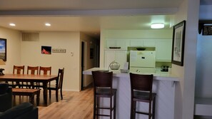 A dining area with a wooden table and chairs, a kitchen with white cabinets, and a sign on the wall.