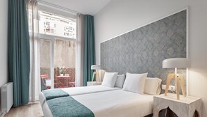 Habitación de hotel con una cama grande, dos mesitas de noche, vistas a la ciudad y un balcón con mesa y sillas.