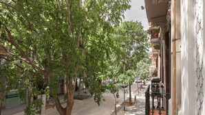 Una calle bordeada de árboles con un edificio que tiene un balcón con barandillas ornamentales.