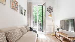 Una sala de estar moderna con un sofá, un televisor, una lámpara y una ventana con vistas a follaje.