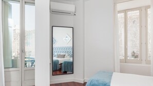 A hotel room with a wooden floor, a bed with a blue blanket, a large window with a view of the city, and an air conditioning unit on the wall. - ART HOUSE CITY CENTRE UNIVERSITAT (BARCELONA)