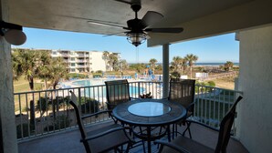 A balcony with a glass-top table and chairs, overlooking a pool and a beach. - CRC 1205 - Beach Getaway for the Whole Family! Ocean View Condo (Saint Augustine)