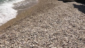 Uma praia rochosa com águas azul-claras e uma colina ao longe.