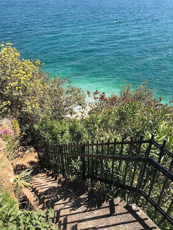 A staircase leading down to a beach with clear blue water.