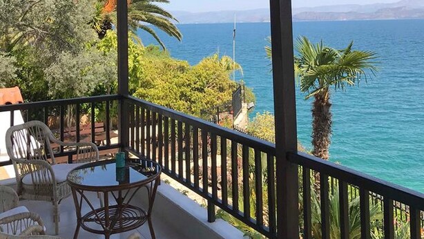 Área externa coberta com vista para o mar, com mesa e cadeiras.