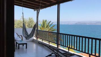 A covered outdoor area with a hammock, chairs, and a view of the sea.