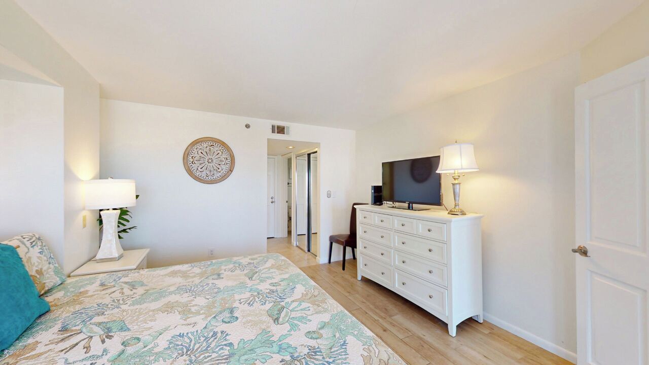 A bedroom with a bed, dresser, TV, and a door leading to another room.