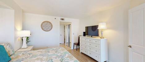 A bedroom with a bed, dresser, TV, and a door leading to another room.