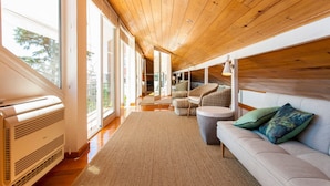 A modern living room with a wooden ceiling, large windows, a sofa, and a small table. - Santos River View Terrace - Boutique Duplex (Lisboa)