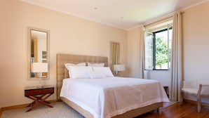 A bedroom with a large bed, a nightstand, a chair, and a window with curtains. - Santos River View Terrace - Boutique Duplex (Lisboa)