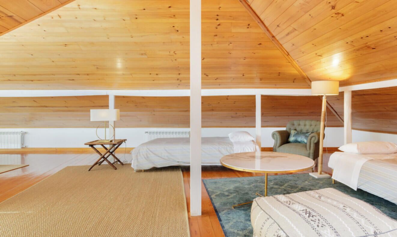 A spacious attic bedroom with wooden ceilings, a round table, two beds, and a chair.