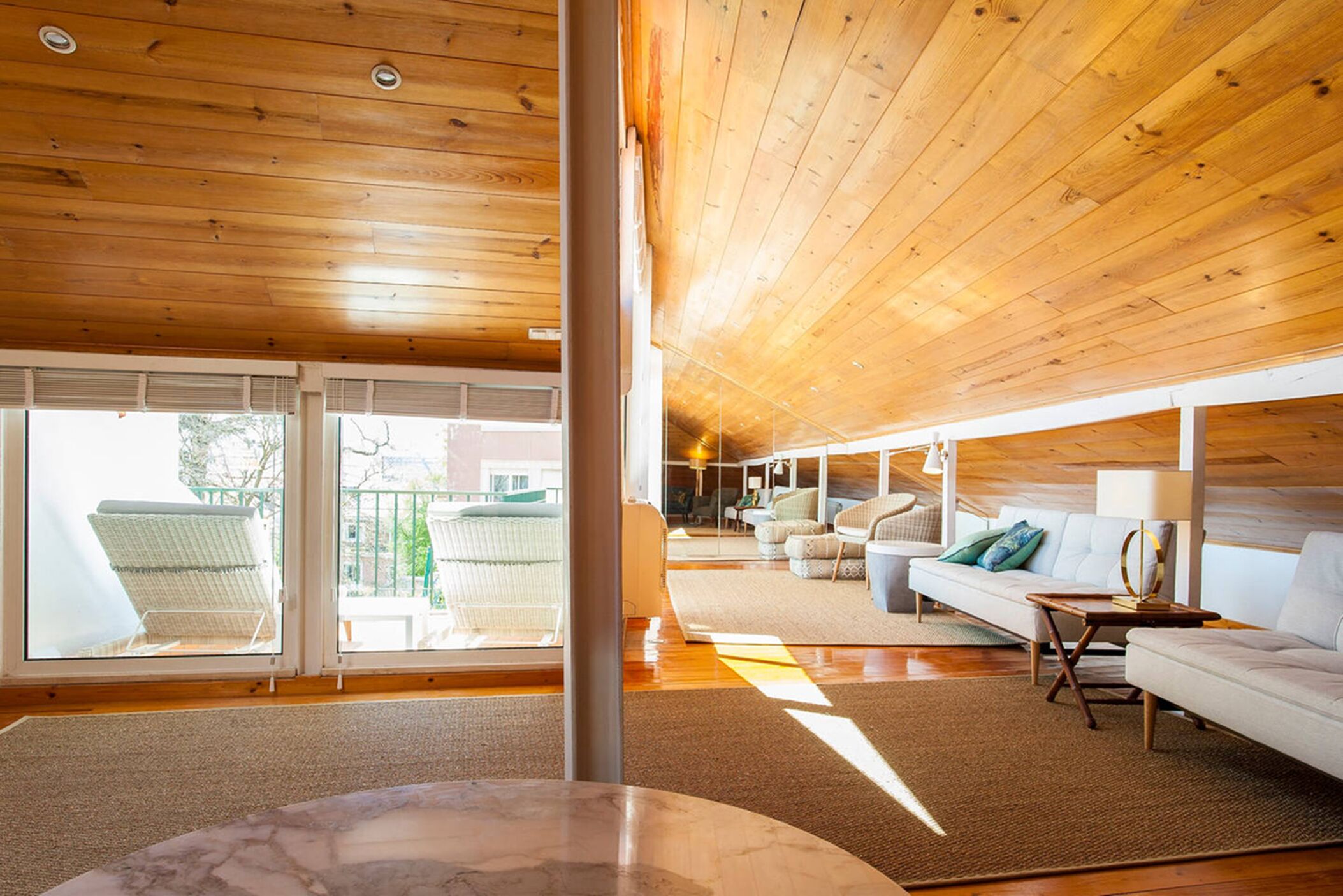 A spacious living area with a wooden ceiling, large windows, and a sofa set.