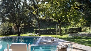 Una piscina con maderas, sillas de descanso y una pared de piedra en un jardín ajardinado.