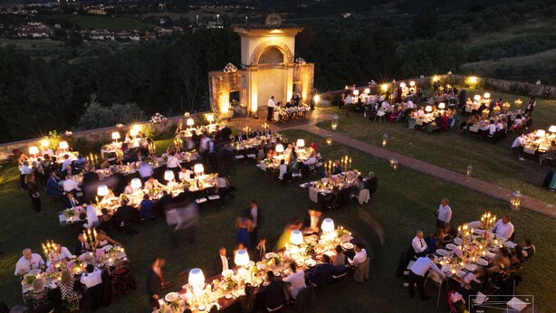 Un área de comedor al aire libre con varias mesas dispuestas para comensales, rodeada de vegetación y una estructura de piedra al fondo.