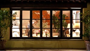 Una ventana tradicional japonesa con varios paneles, plantas en macetas a cada lado y vista a una habitación con muebles y una lámpara.