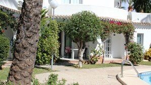 Ein Innenhof mit Pool, umgeben von einem weißen Gebäude mit einem Ziegeldach, einer Palme und verschiedenen Sträuchern.
