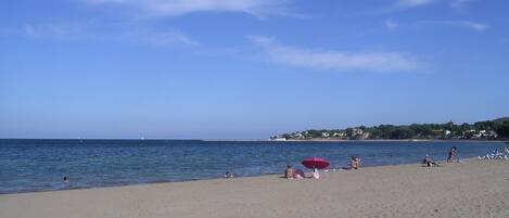 A beach with a wooden boardwalk, people relaxing, and a clear blue sky.