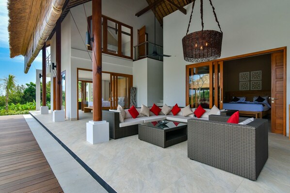 A modern outdoor lounge area with wicker furniture, a glass coffee table, and a hanging light fixture.