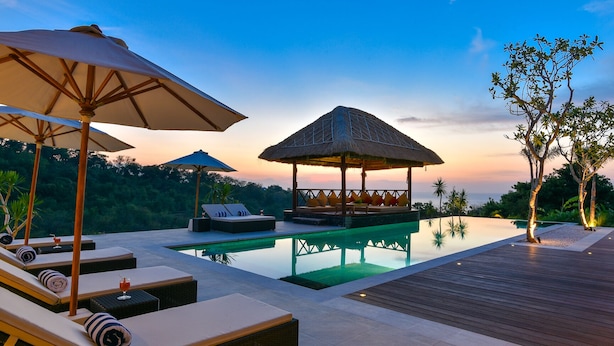 A serene poolside area with lounge chairs, umbrellas, and a thatched-roof structure.