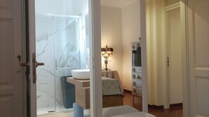 A hotel room with a large bed, a bathroom with a glass shower, and a sitting area with a lamp.