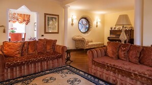 A living room with two sofas, a patterned rug, a round mirror, and a piano.