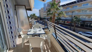 Un balcon avec une table et des chaises, donnant sur une rue animée où l’on peut voir des voitures et des immeubles.