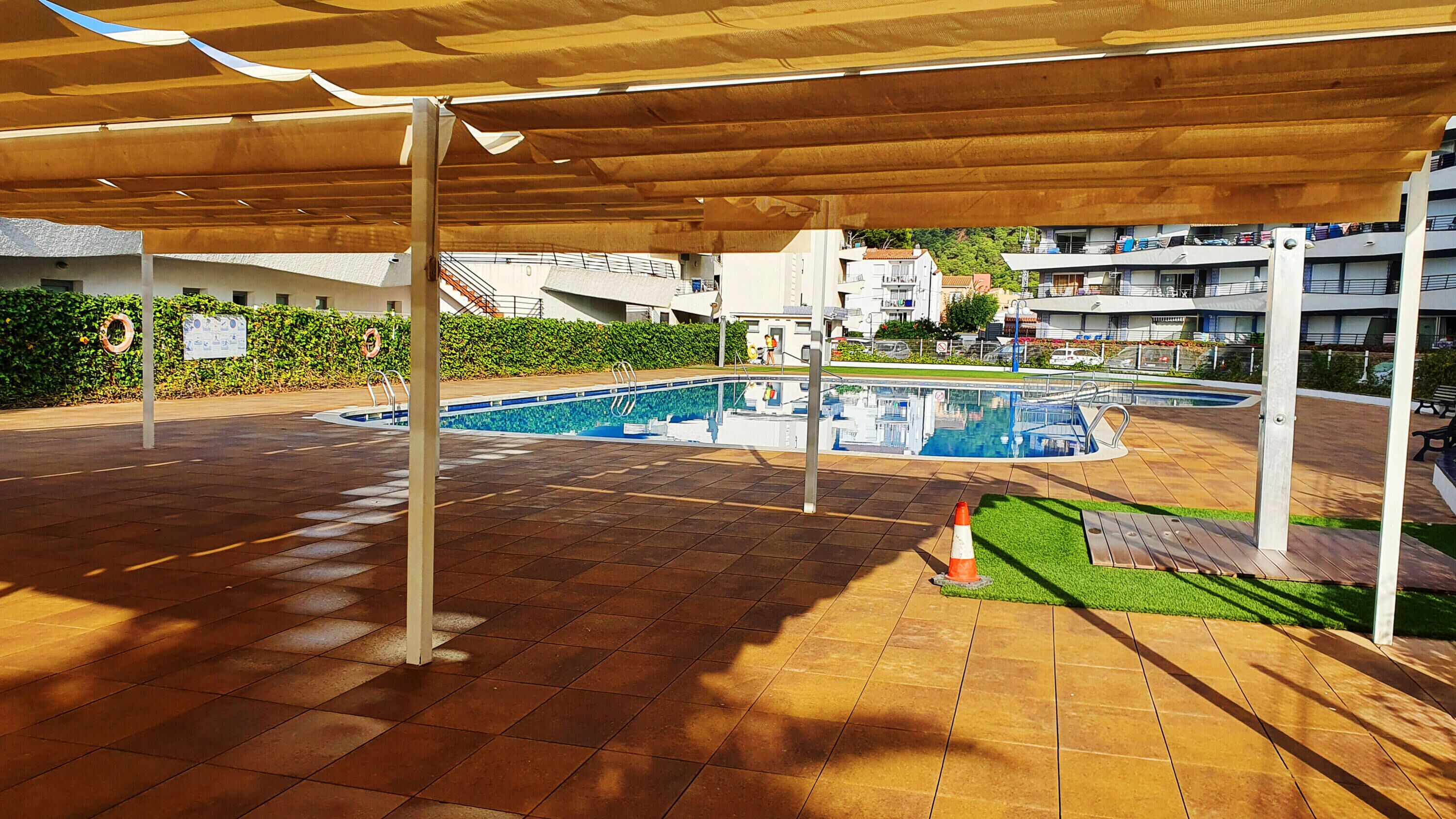An outdoor swimming pool area with a covered patio, a lifeguard stand, and a small grassy area.
