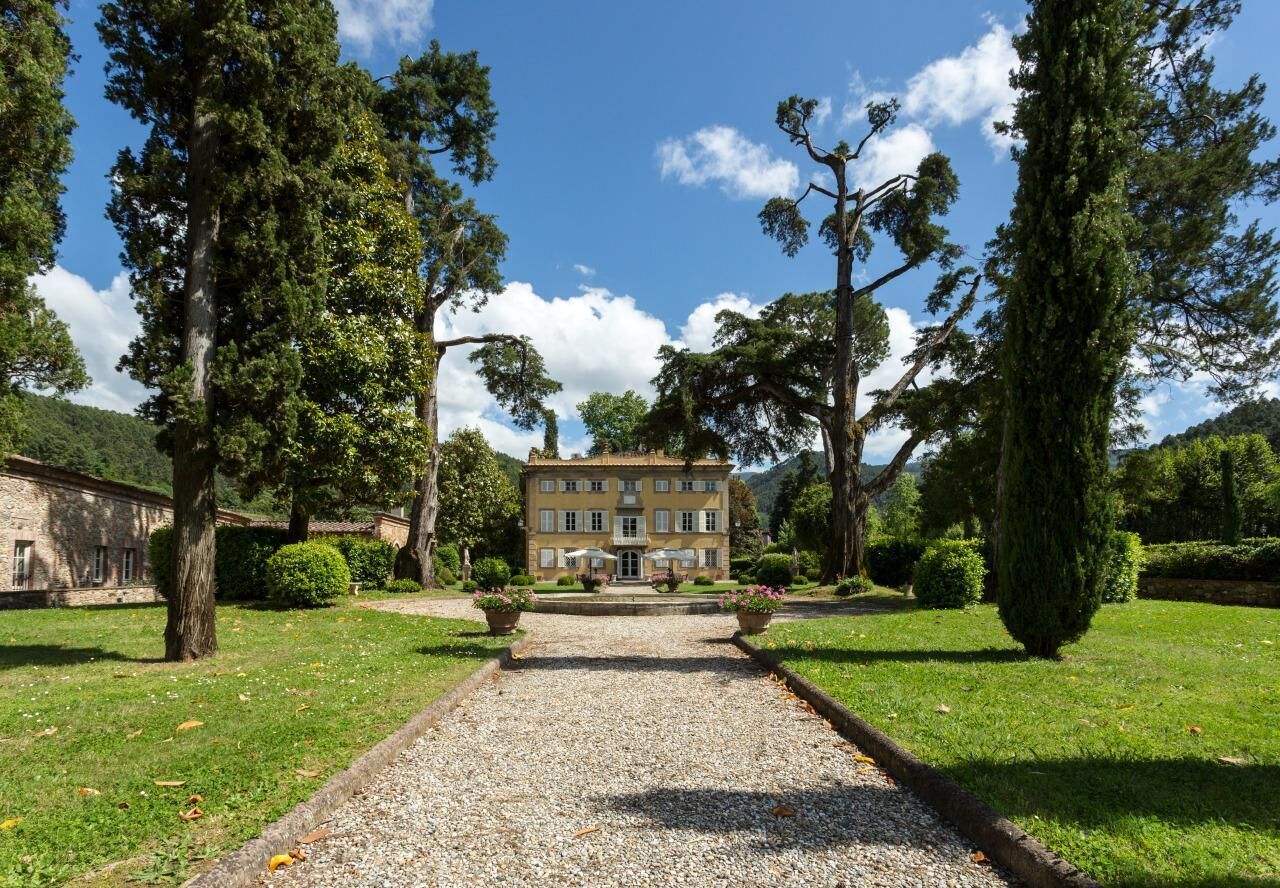 A building with a symmetrical facade, a gravel pathway leading to the entrance, and surrounding greenery.